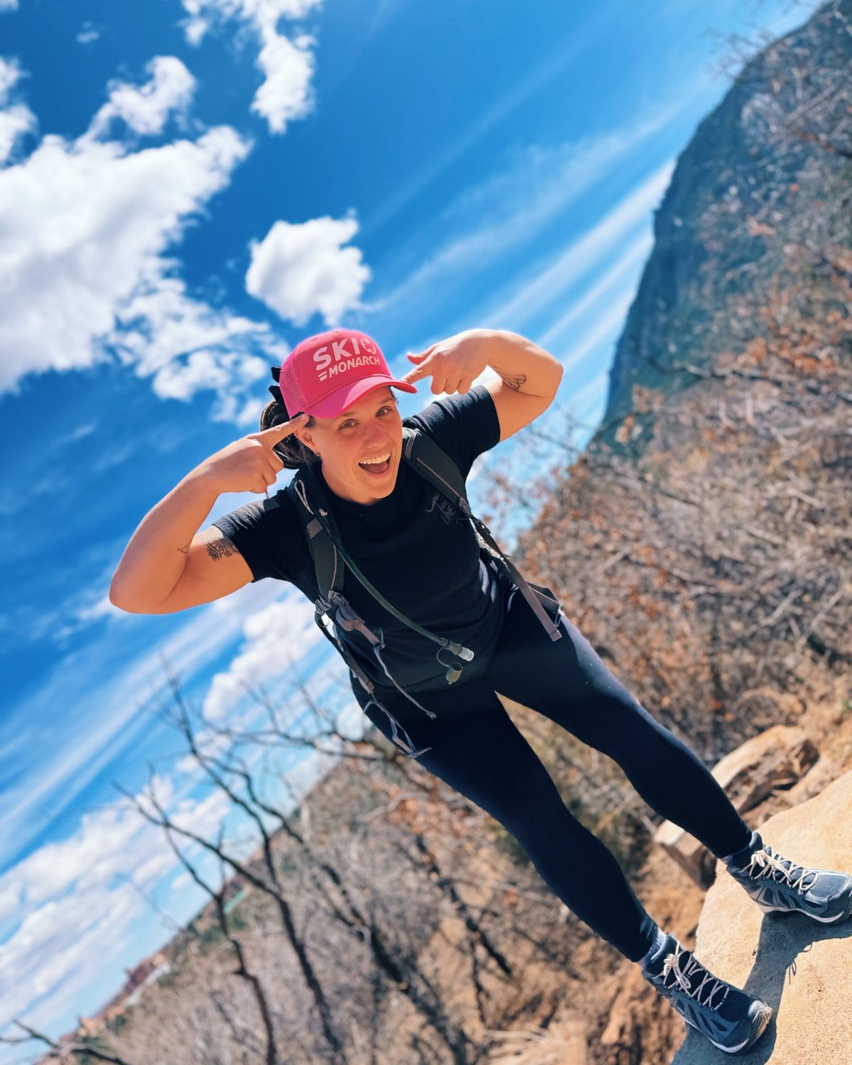 Cass Dinsmore on a mountain trail, laughing and pointing at her pink Ski Monarch cap